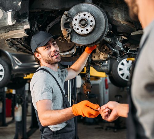 professional manual workers repairing car without wheel in mechanic shop